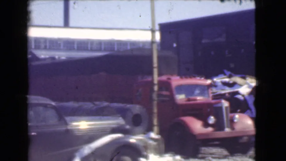 A dark vintage sedan passes or sits in the foreground while the red truck remains near the snowy factory lot in Cleveland.