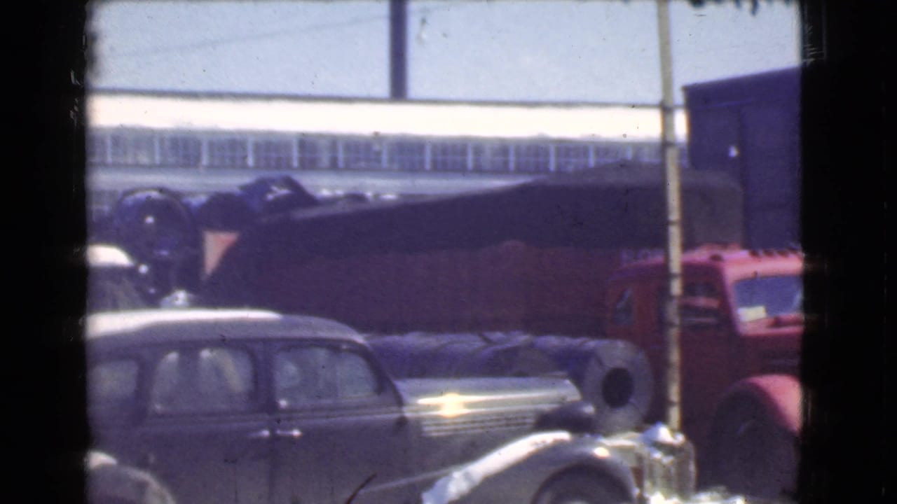 1939 Cleveland yard view with older automobiles, a red truck, and warehouse siding in soft 8mm color.