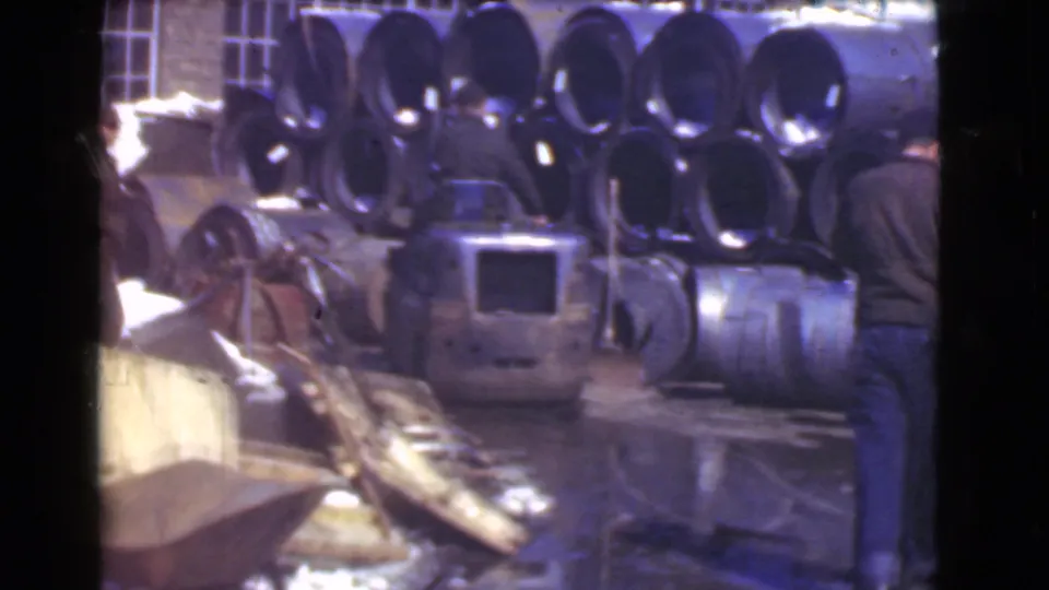 Cleveland, 1939 factory yard scene with workers beside stacked metal pipes, machinery, and wet ground in 8mm footage.