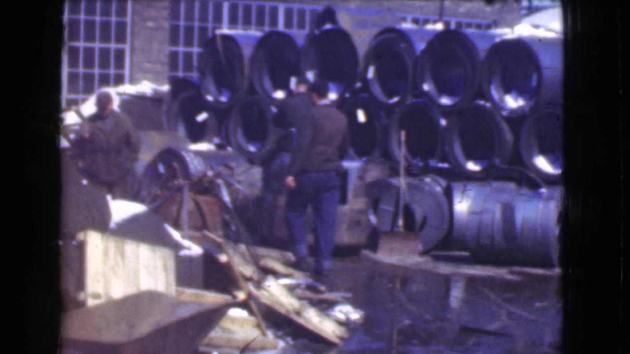 Cleveland, Ohio 1939 8mm footage appears to show workers around a small forklift near stacked metal cylinders on a wet industrial floor.