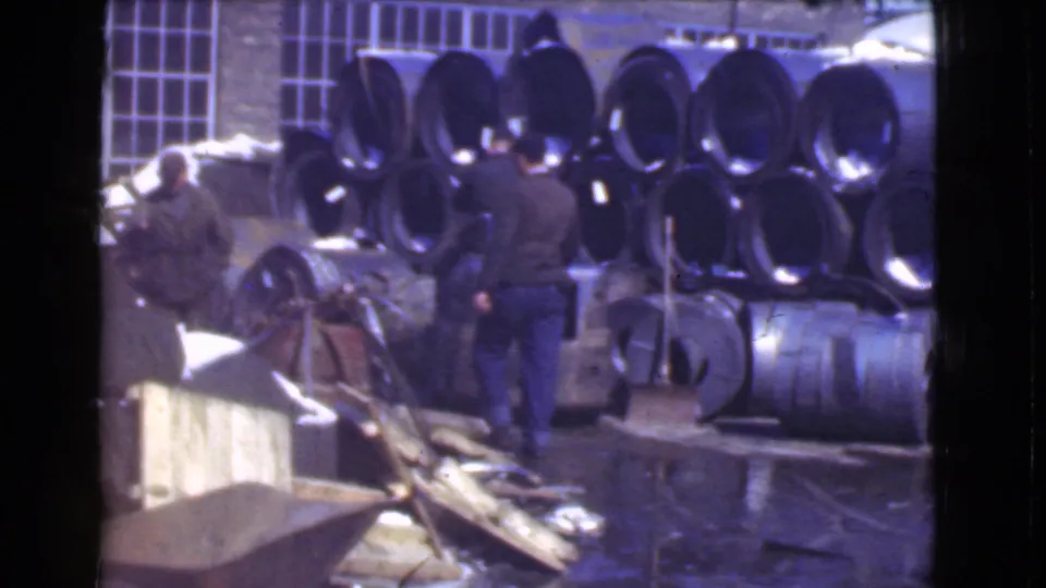 Cleveland, Ohio 1939 8mm footage appears to show workers around a small forklift near stacked metal cylinders on a wet industrial floor.