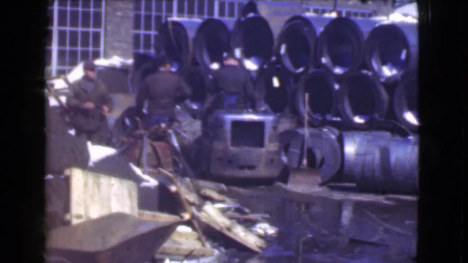 A small forklift sits near adult workers and rows of stacked metal pipe or coils in Cleveland industrial footage from 1939.
