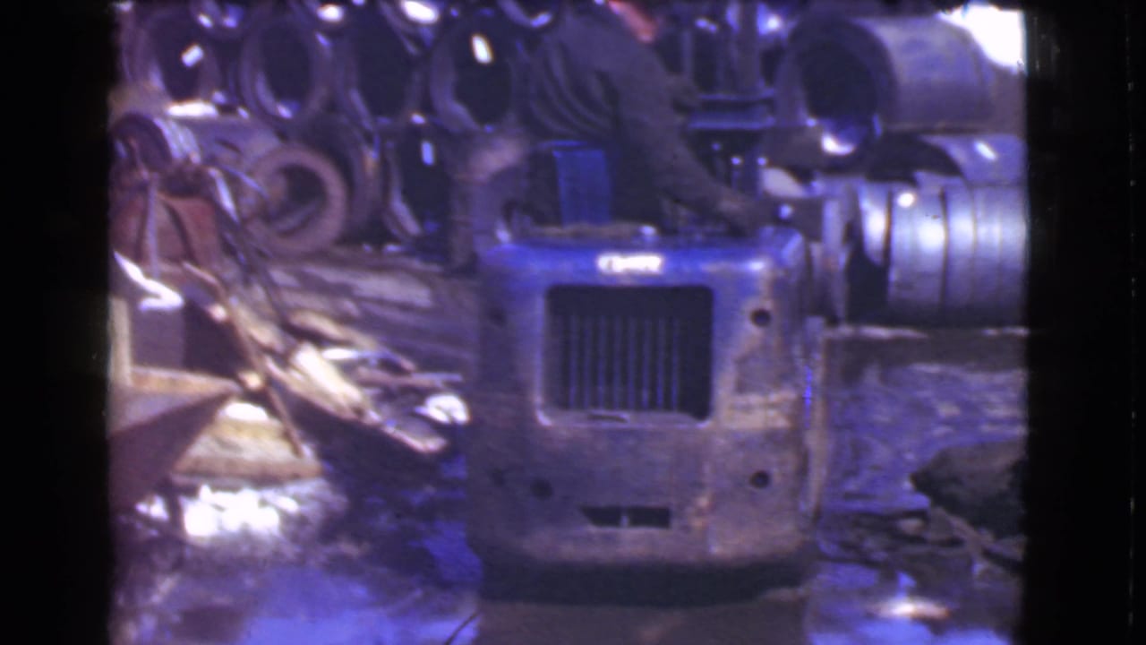 1939 Cleveland industrial home-movie frame showing the front grille of a blue forklift surrounded by metal parts and warehouse materials.