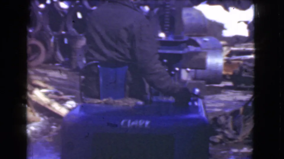 A man operates a blue forklift in a Cleveland industrial setting, with stacked materials and machinery visible around the vehicle.