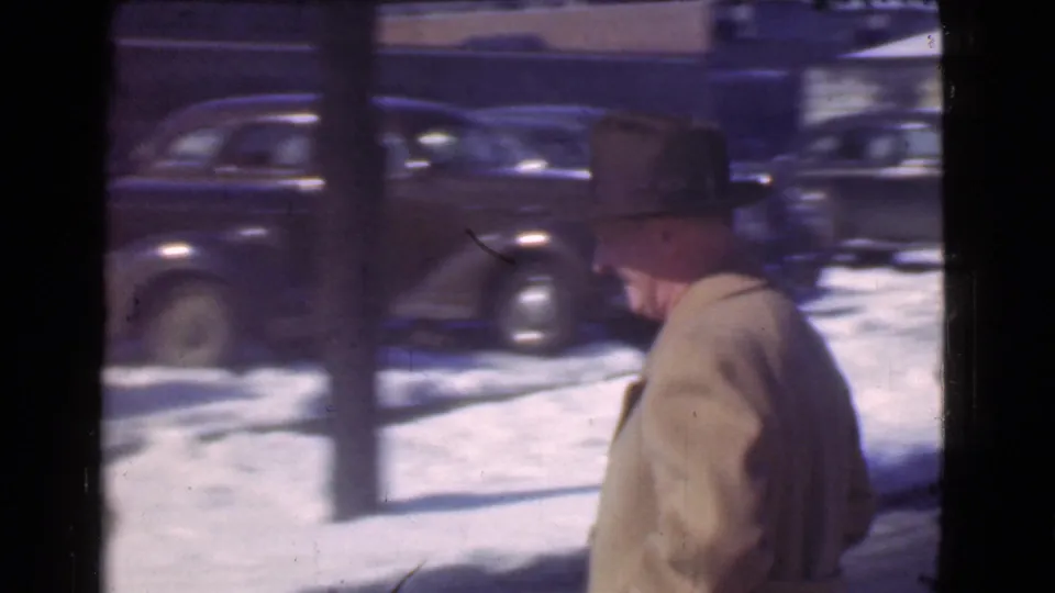 The same man continues along a snowy Cleveland street as dark 1930s automobiles line the opposite curb.