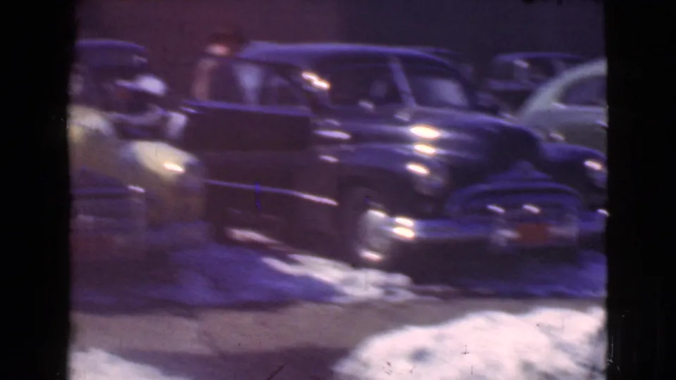 A dark 1930s sedan sits among other parked cars on a snow-covered Cleveland street in the home-movie footage.