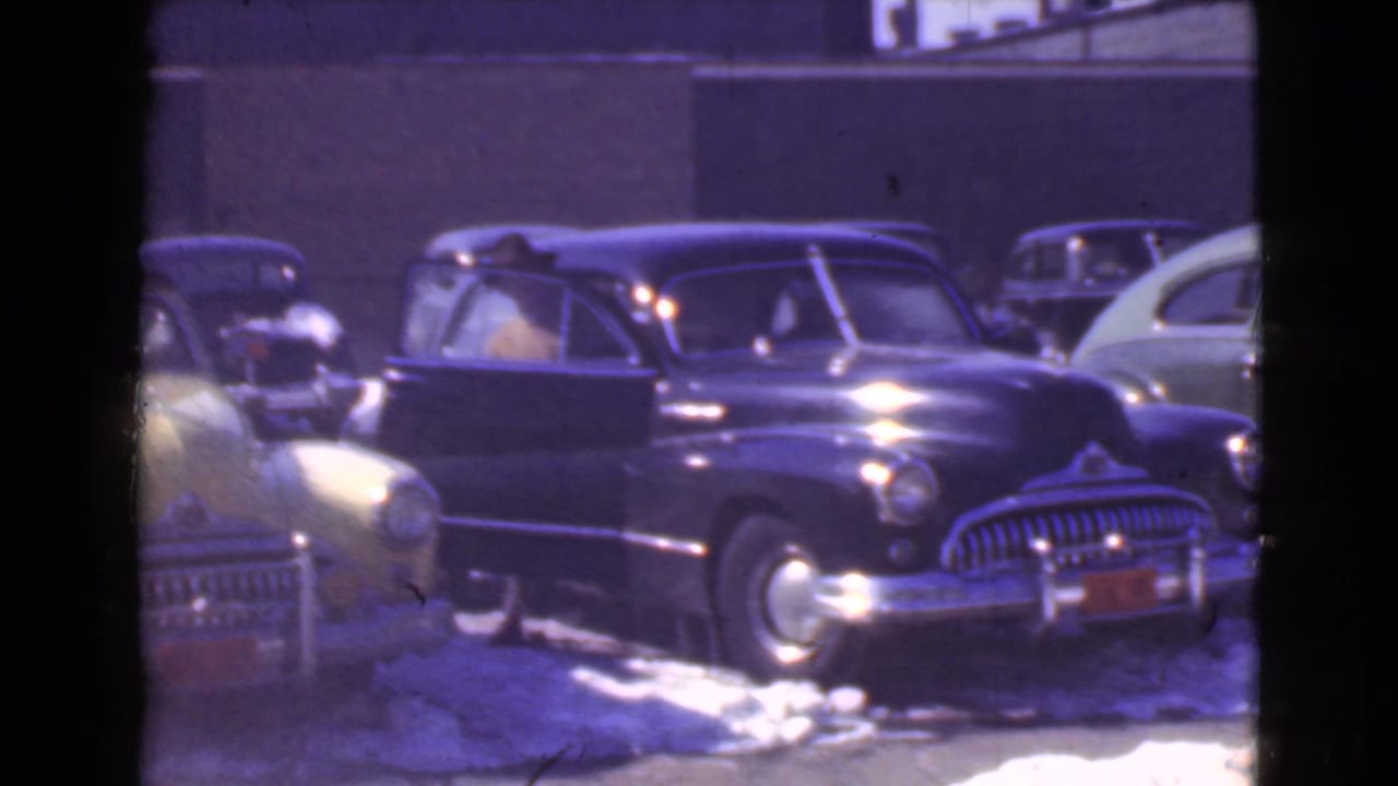 Dark vintage car parked on a snowy street with other period automobiles nearby.
