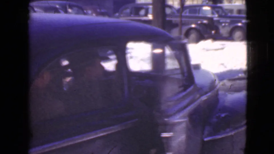 A dark 1930s sedan dominates the frame in the snowy Cleveland parking area, with other parked cars visible in the background.