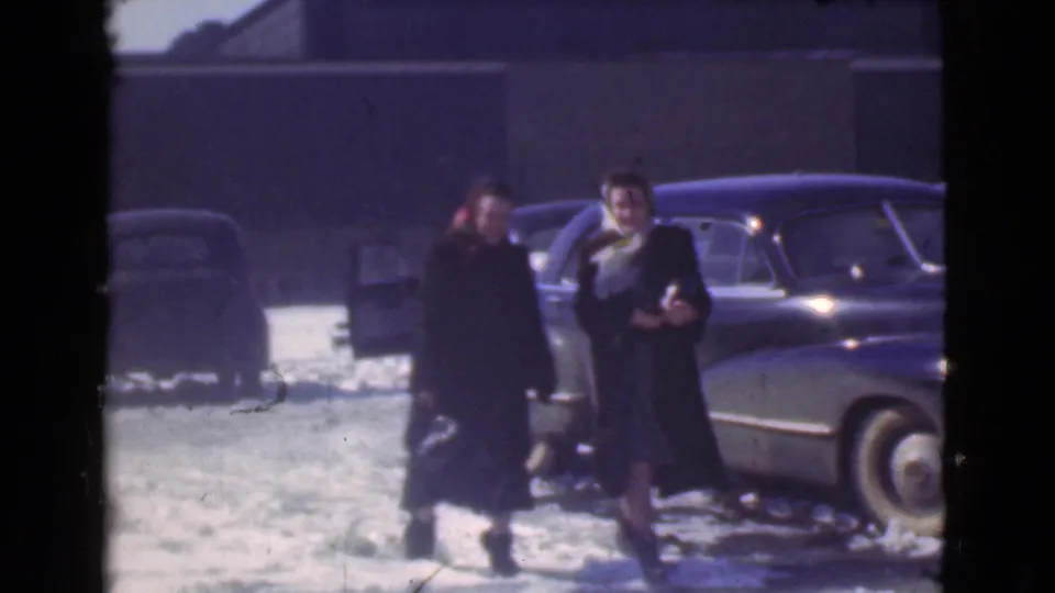 The two women continue across the snowy 1939 Cleveland parking lot, passing a parked car while looking generally toward the camera.