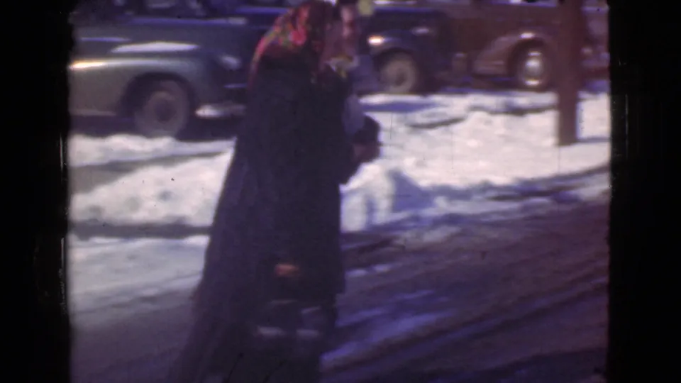 The women continue away from the camera along a snowy Cleveland street, framed by parked automobiles and winter light in 8mm home-movie footage.