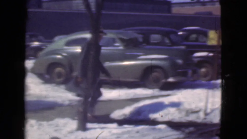 Cleveland, Ohio street in 1939 with snowbanks, bare trees, parked vintage cars, and a blurred pedestrian moving through the frame.
