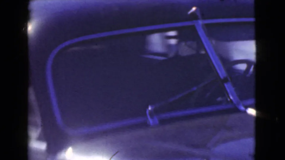Close-up of the vintage car's side window, windshield frame, and dark interior in the Cleveland street footage.