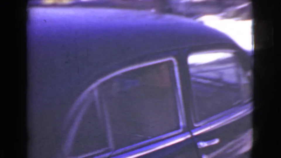 Home-movie close-up of the vintage sedan's side door, roof, window trim, and snowy street edge.