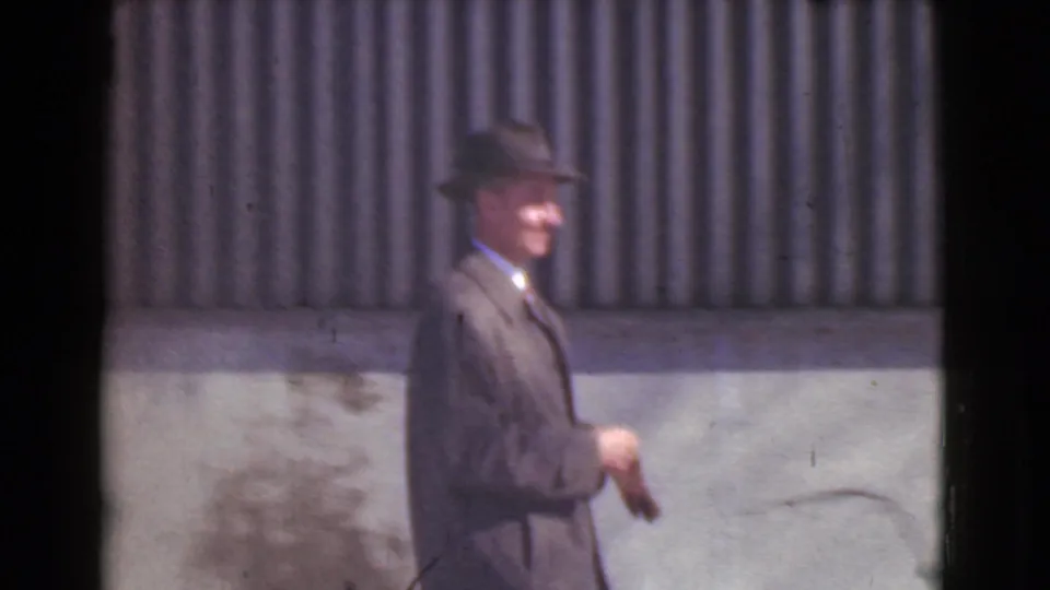 A smiling suited man in a fedora walks in profile outside a Cleveland building in the 1939 home movie.