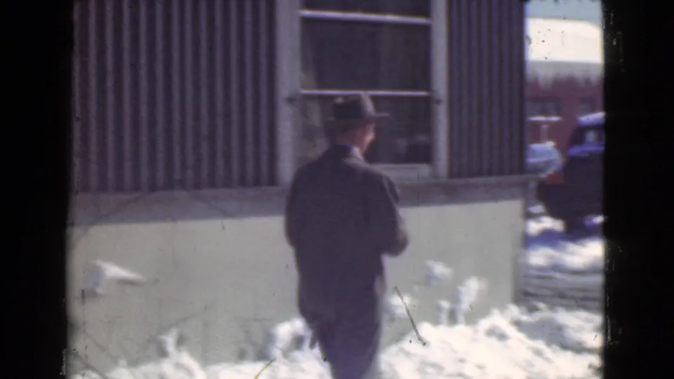 The man is seen from behind walking along a snow-covered Cleveland street beside a corrugated exterior wall.