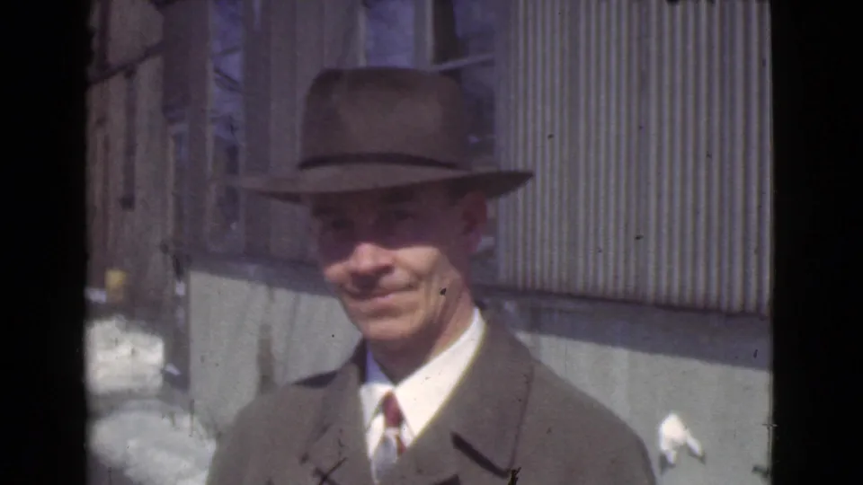Close view of the adult man in fedora, suit, tie, and overcoat near the corrugated building in snowy 1939 Cleveland footage.