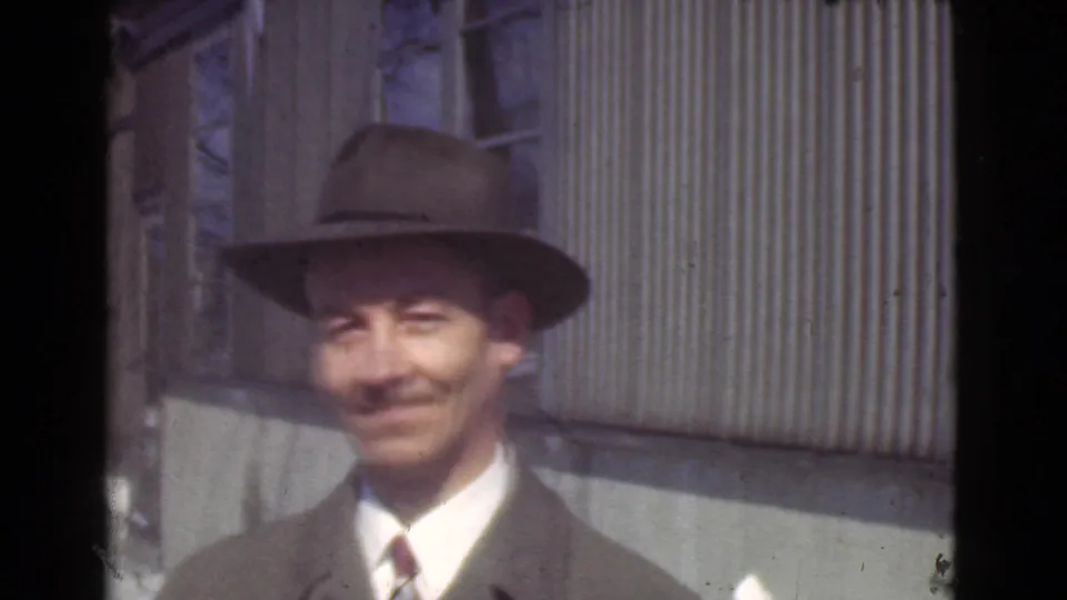 Adult man in 1939 Cleveland home-movie footage smiles toward the camera while wearing a fedora, suit, tie, and overcoat.