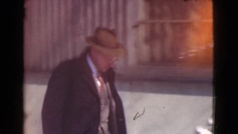 In 1939 Cleveland home-movie footage, a man in a dark overcoat and fedora walks near a snow-covered sidewalk.