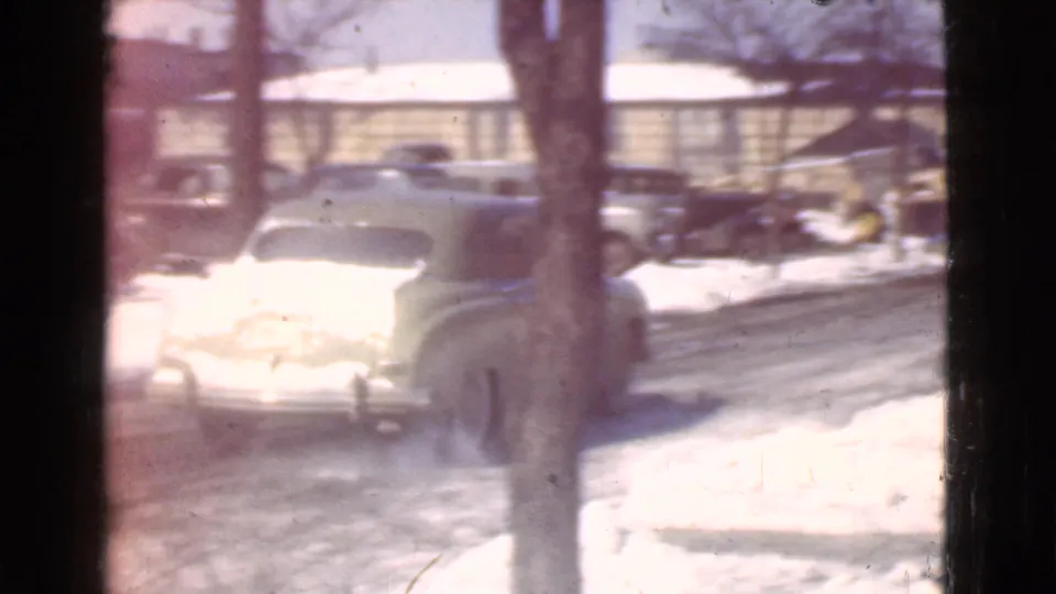 A snowy Cleveland street scene shows period cars, bare trees, and a bundled pedestrian near a sign post.