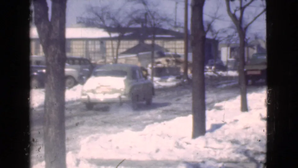 The frame shows a winter Cleveland street with snowbanks, late-1930s cars, bare trees, and low buildings in the background.