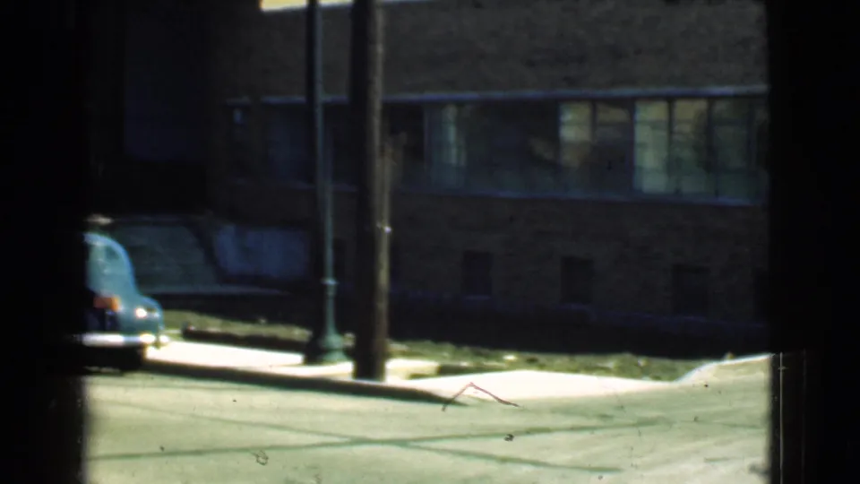 A Cleveland street view shows a brick building, sidewalk, utility or streetlight poles, and a rounded 1930s automobile near the curb.