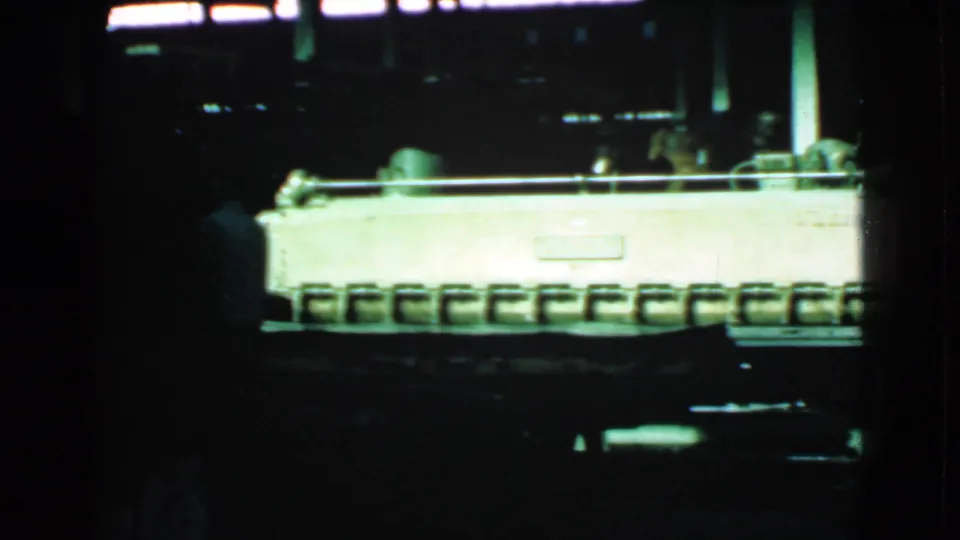 The frame shows a long illuminated machine or conveyor with a person in shadow at the left, consistent with the Cleveland 1939 metadata.
