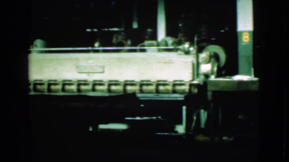 Final 1939 Cleveland frame with a bright machine or conveyor, a vertical support, and dark industrial surroundings.