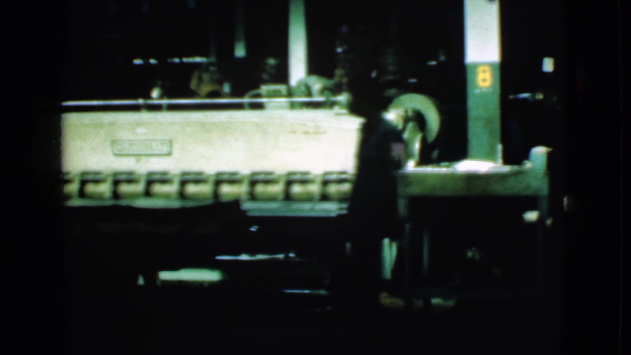 1939 Cleveland factory interior showing heavy machinery in low light with a silhouetted worker moving near the equipment.