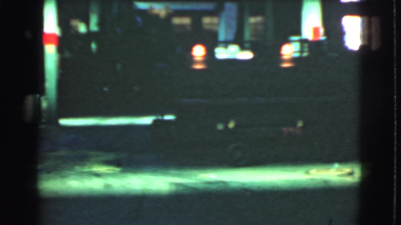 1939 Cleveland home-movie frame showing a dim night street near bright service-station lighting and vehicle lights.