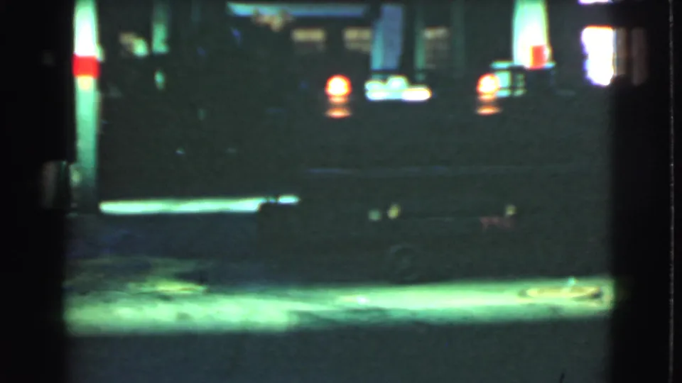 1939 Cleveland home-movie frame showing a dim night street near bright service-station lighting and vehicle lights.