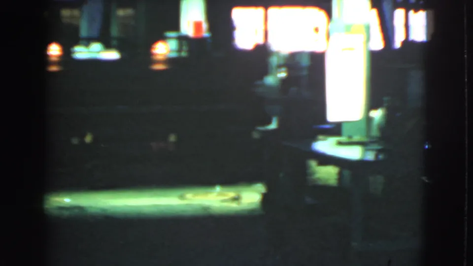 Low-light 8mm frame of a Cleveland street near a glowing service-station area, with heavy shadow and lamp bloom.