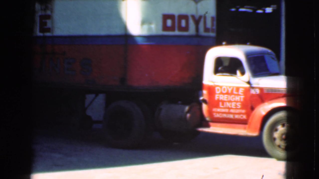 Red and white Doyle Freight Lines truck passing a loading area.