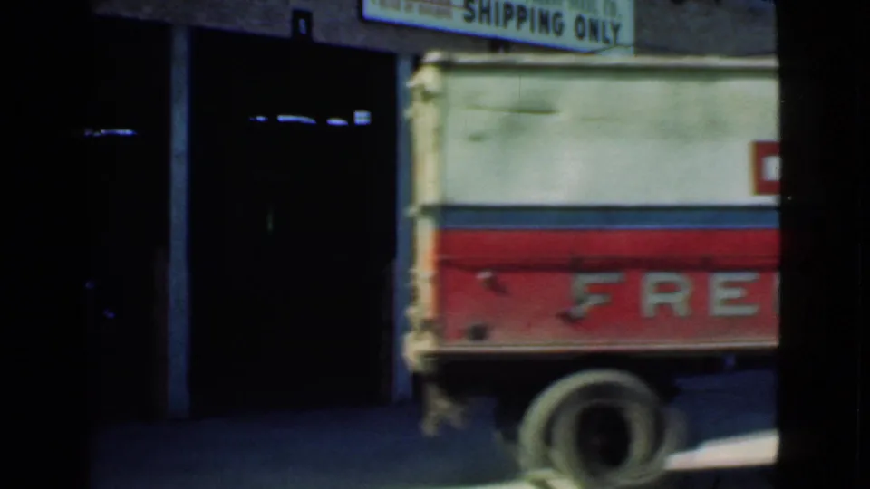 1939 Cleveland frame showing the rear portion of a Doyle freight truck moving past dark loading dock openings and shipping signage.