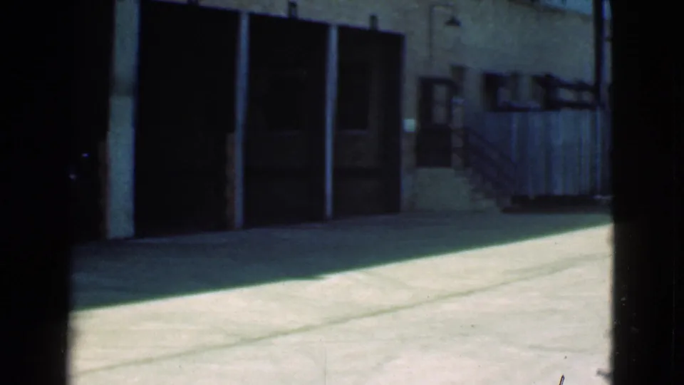 Roaming 8mm view in Cleveland, Ohio, with garage bays, brick exterior, concrete alley pavement, fencing, and stairs at the right.