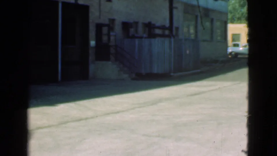 Final 1939 Cleveland alley frame with garage frontage, fencing, stairs, bright pavement, and a classic car briefly visible in the distance.
