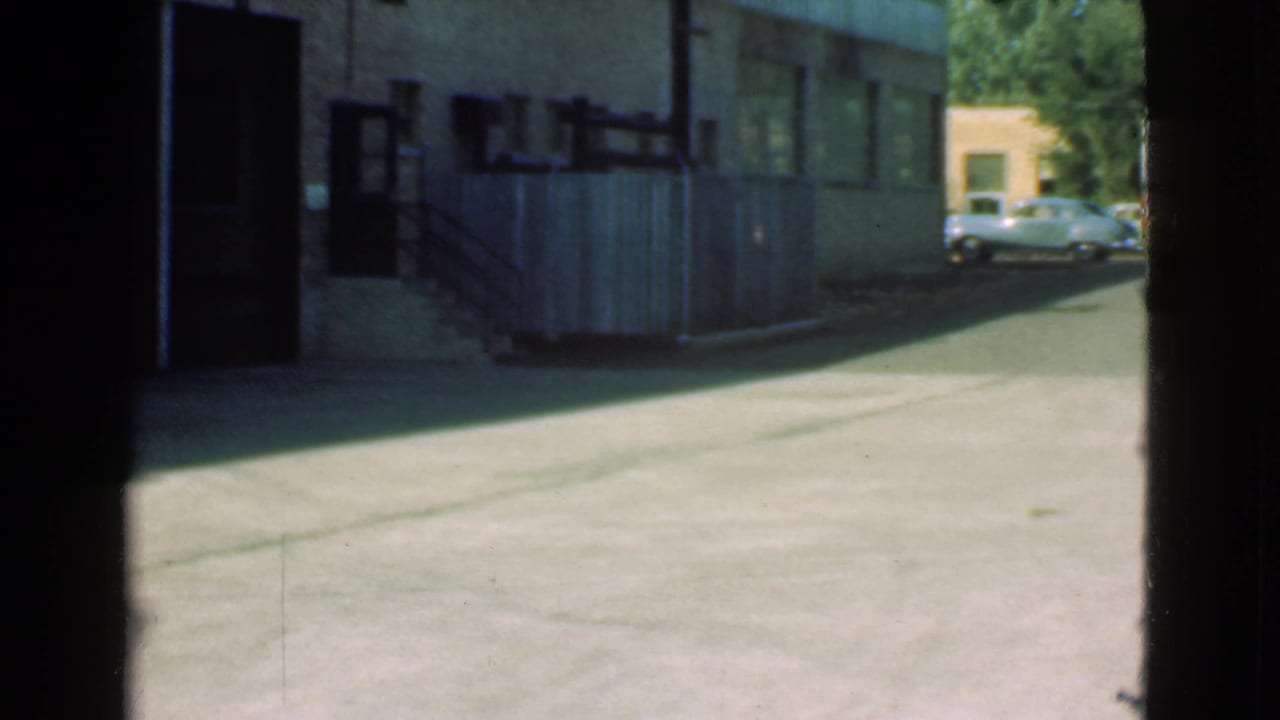 Quiet asphalt street seen past dark doorway edges with buildings and parked cars in the distance.
