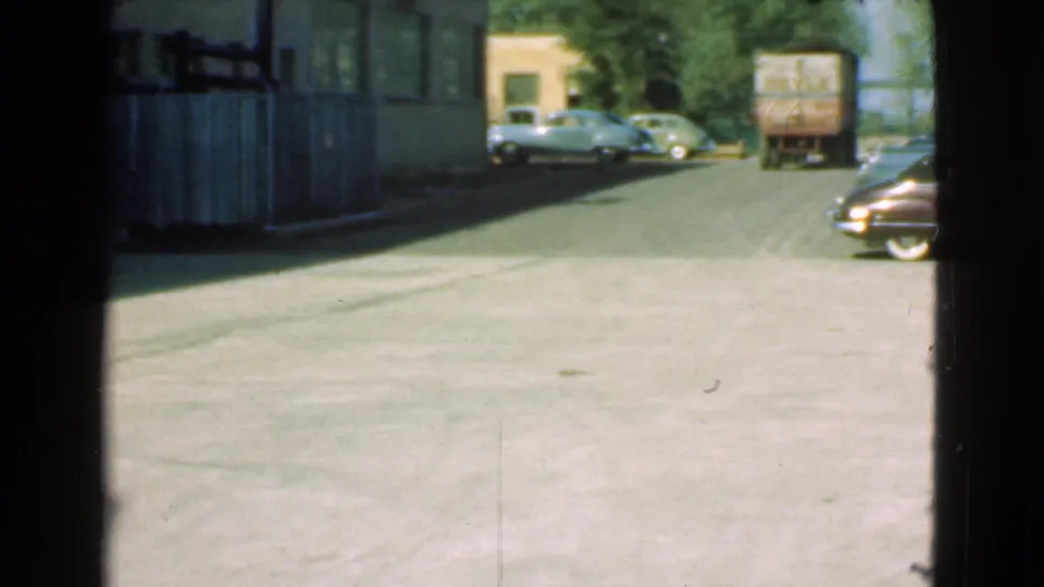 1939 Cleveland street scene with a small lorry in the road, parked rounded sedans, building shadows, and open pavement.