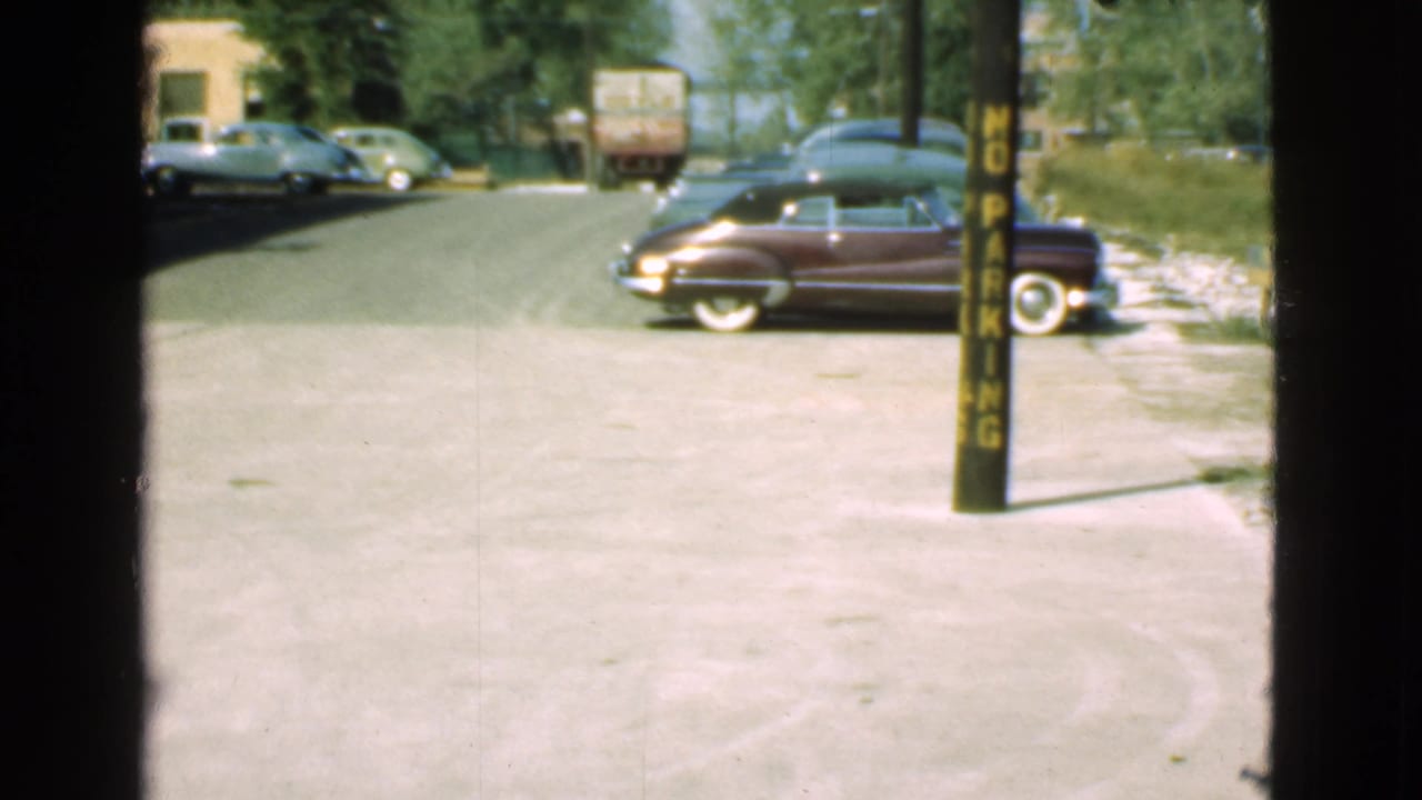 Similar street view with a maroon car, background cars, truck, and no-parking pole.