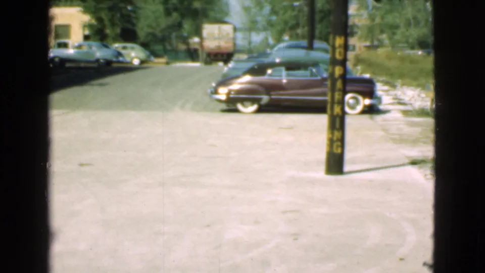 A 1939 Cleveland street scene shows a maroon period car near a yellow no-parking pole with other automobiles and a truck behind it.