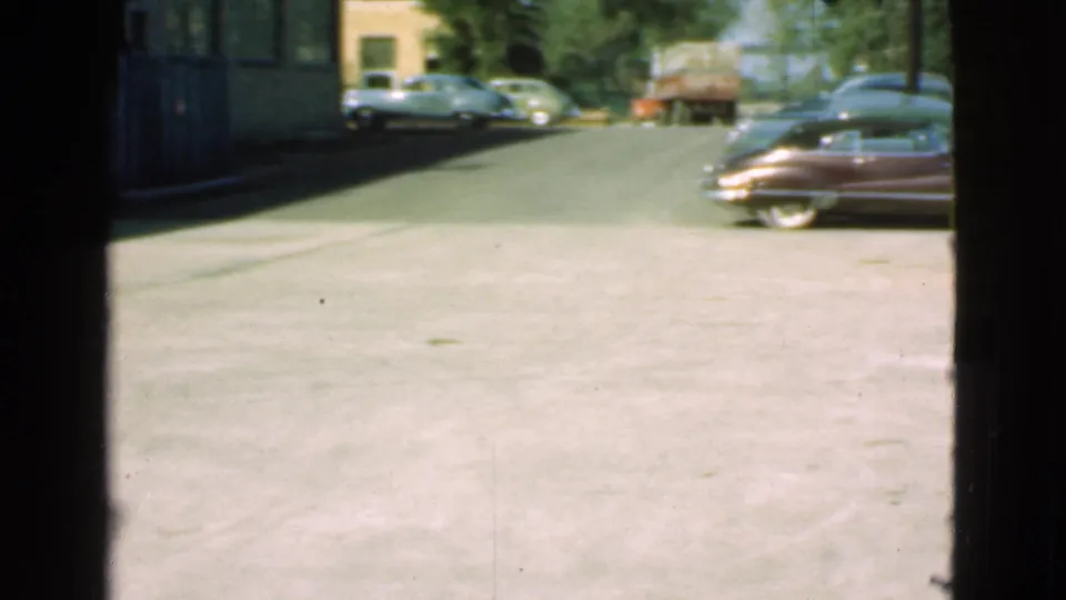 Soft 8mm view of a Cleveland street in 1939 with parked automobiles, a truck, open pavement, and dark frame edges from the camera position.