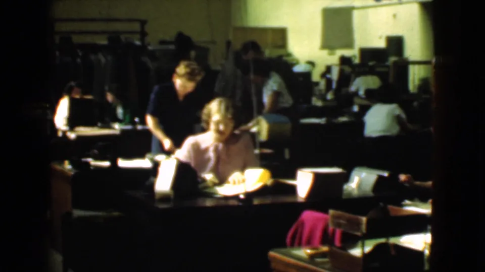 1939 office interior in Cleveland with women working at desks under dim light, surrounded by papers, lamps, chairs, and dark office furniture.