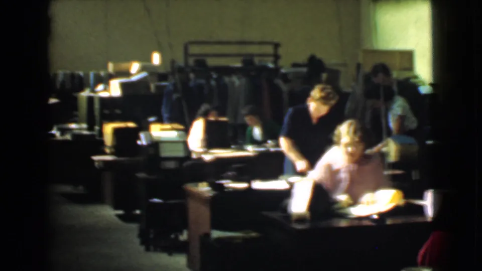 Several women are visible among desks, lamps and clothing racks in a Cleveland factory office identified by metadata as 1939.