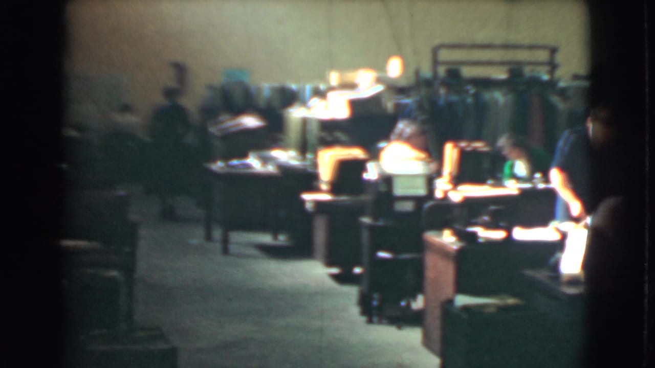 Workers seated at desks under bright lamps in a large office interior.