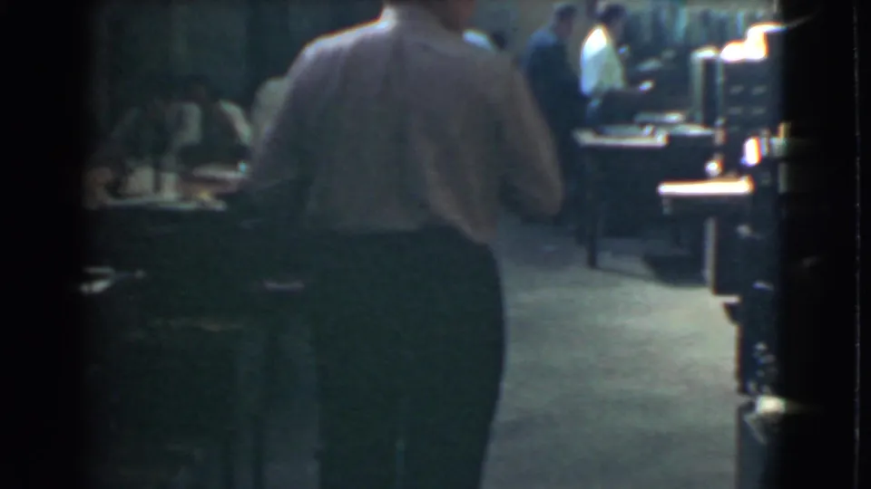 A man in a light shirt is seen from behind among desks and workers in the 1939 Cleveland office interior.