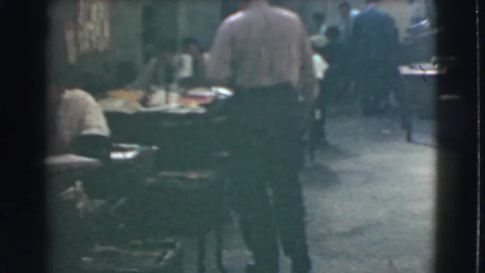 Final office view with a man in a light shirt standing among desks, workers, chairs, and dim interior lighting in Cleveland, 1939.