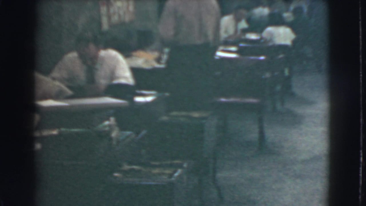 Office workers seated at desks with papers in a dim interior.