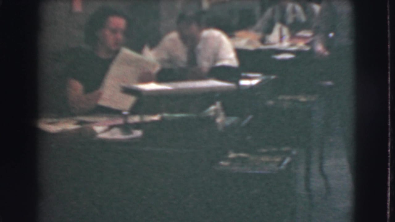 Office workers sit at desks with papers spread across the work area.