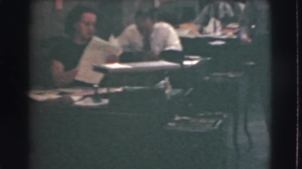 1939 Cleveland office interior with workers seated at desks, papers in hand, and rows of workstations visible in low light.