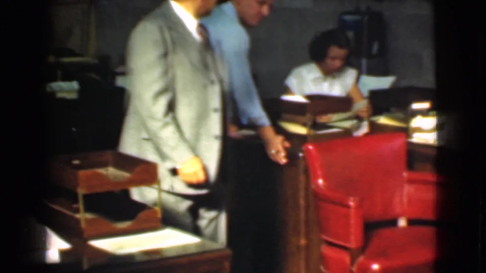 1939 Cleveland office interior showing suited men near a desk and a woman working with papers in the background.