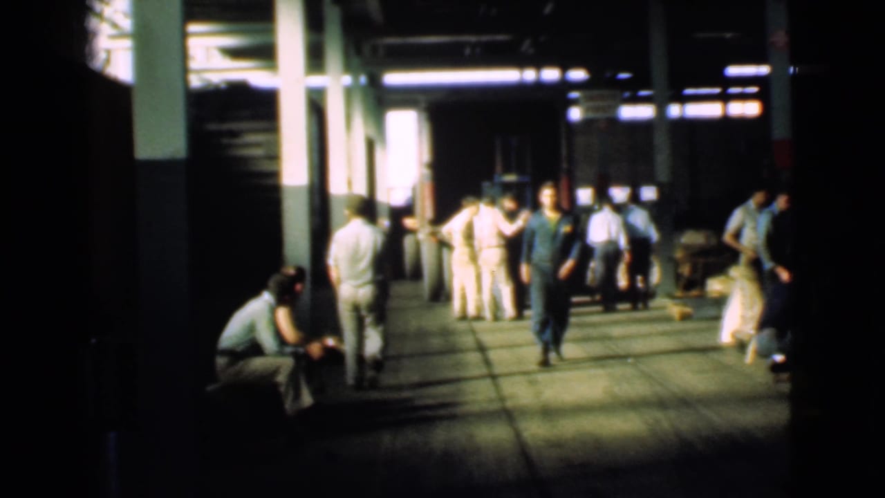 Workers inside a Cleveland industrial corridor in 1939, with a man in dark clothing walking toward the camera and others gathered near columns.